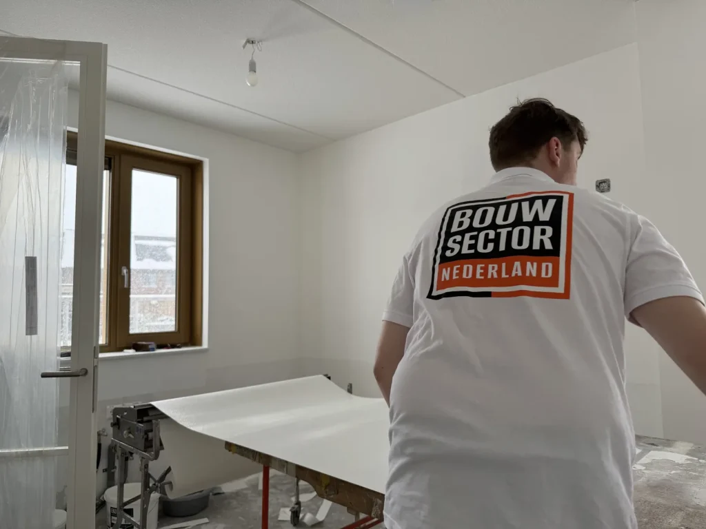 Vakman van Bouwsector Nederland rolt een baan vlies uit over de plaktafel naast een raam met houten kozijn