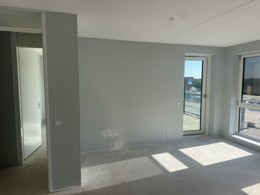 Nieuw appartement met lichtgrijze wanden, een betonvloer en een balkondeur