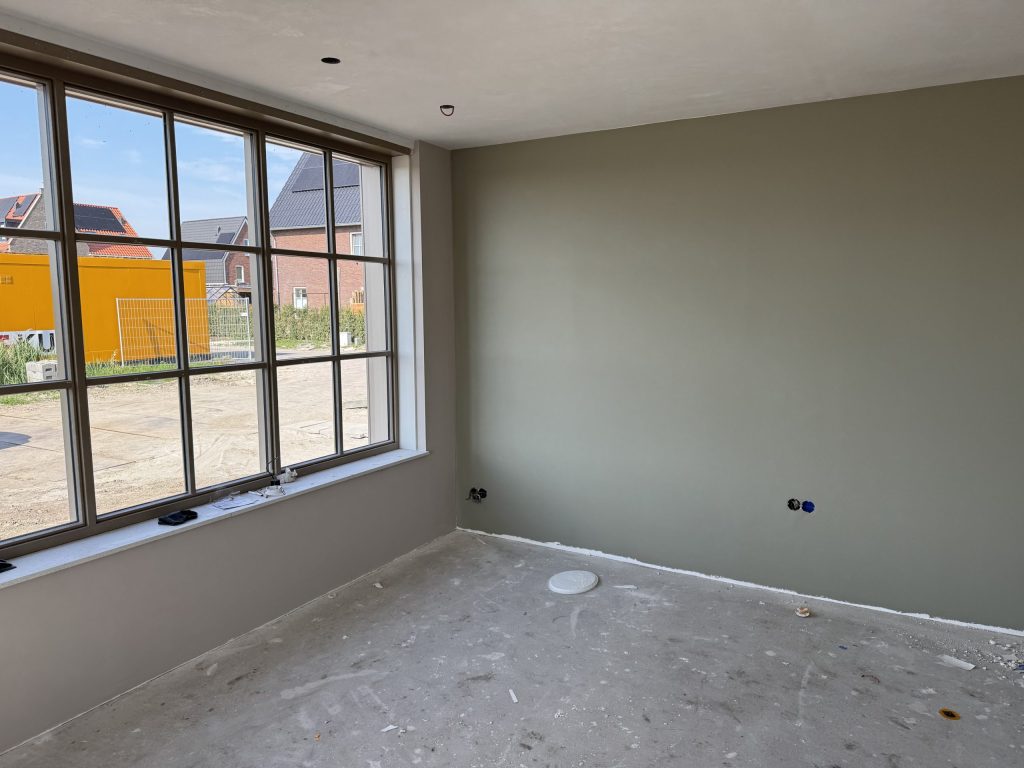 Kamer in een nieuwbouwhuis met een egale grijsgroene wand en een groot raam