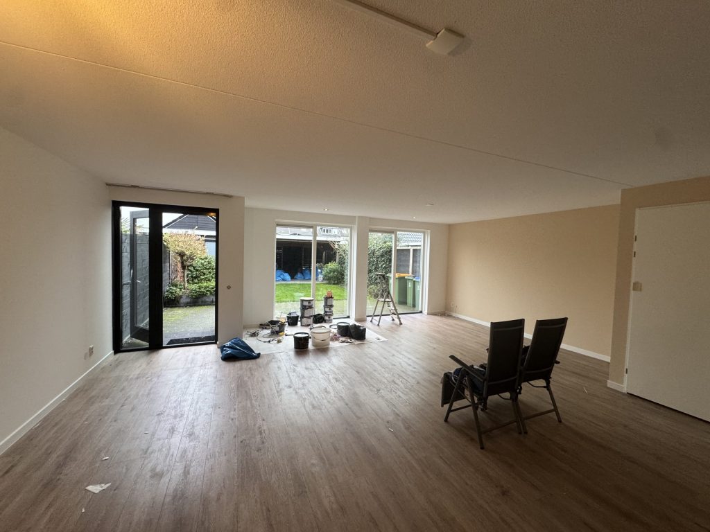 Ruime woonkamer met lichte, gesausde wanden, een houten vloer en tuindeuren naar de achtertuin