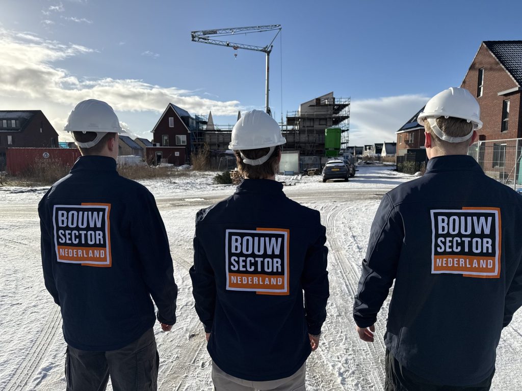 Drie collega's van Bouwsector Nederland met bouwhelm op een besneeuwde bouwplaats met nieuwe woningen